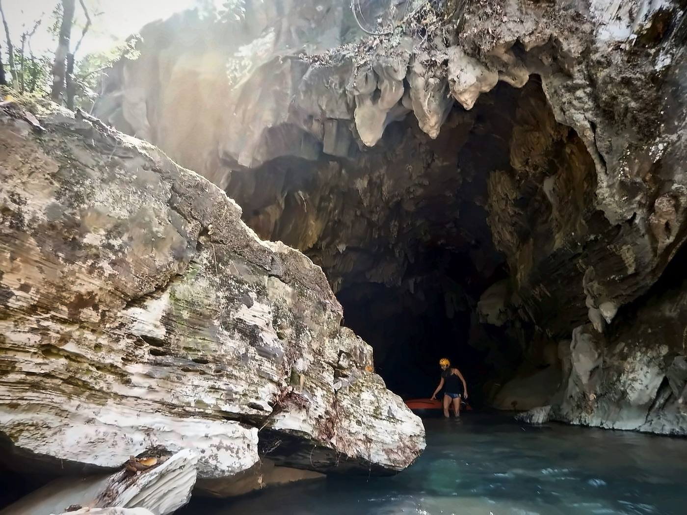 Pessoa com capacete e boia na entrada de uma caverna com rio